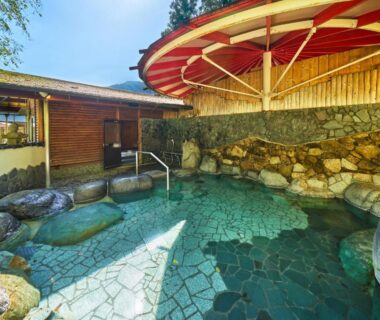 Outdoor stone onsen with wooden bathhouse and umbrella canopy at Ooedo Onsen Monogatari Gero Bekkan, Gifu