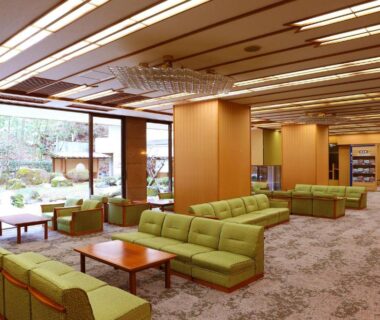 Ryokan lounge with green sofas, low tables and large garden-facing windows at Ooedo Onsen Monogatari Kounkaku in Miyagi