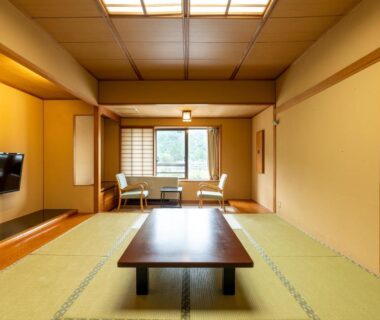 Spacious tatami room with low table, seating by window, wooden paneling and wall-mounted TV at Ooedo Onsen Monogatari in Miyagi