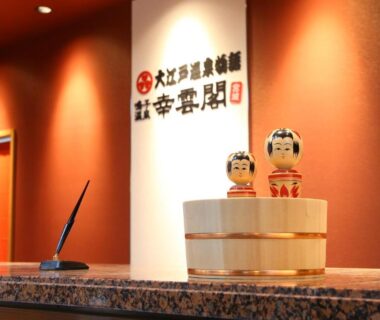 Two kokeshi dolls on a reception counter with ryokan signage at Ooedo Onsen Monogatari Kounkaku, Miyagi