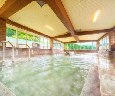 Spacious indoor onsen bath at Ooedo Onsen Monogatari Miyoshiya with handrails and large windows overlooking greenery Hyōgo