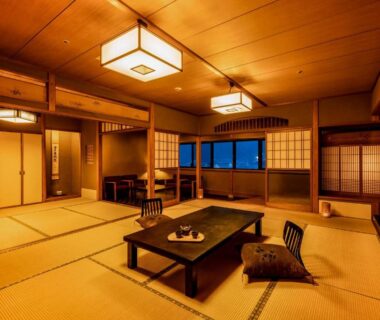Spacious tatami room with low table, cushions, shoji screens and large windows at Ooedo Onsen Monogatari Miyoshiya Hyōgo