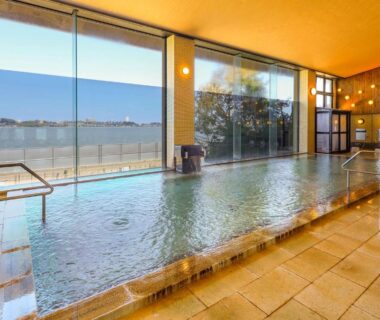 Spacious indoor onsen bath with large windows overlooking waterside at Ooedo Onsen Monogatari Nagayama, Ishikawa