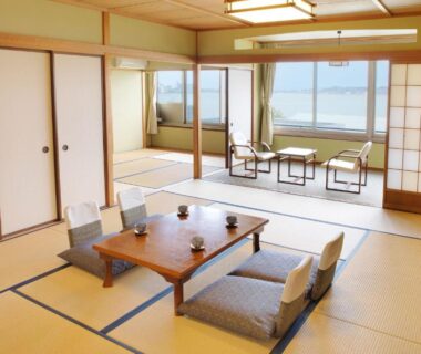 Spacious tatami room with low table, floor cushions, shoji screens and window seating at Ooedo Onsen Monogatari Nagayama, Ishikawa