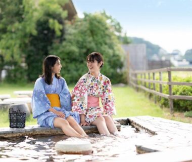 Two women in yukata relaxing at outdoor footbath at Ooedo Onsen Monogatari Nagayama in Ishikawa