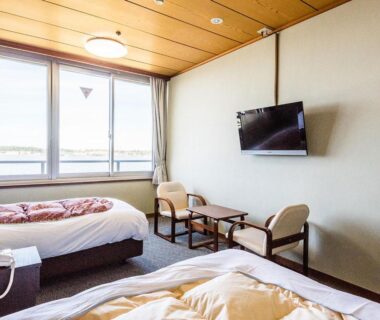 Two beds, wall-mounted TV, seating by window at Ooedo Onsen Monogatari Nagayama in Ishikawa