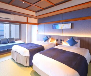 Tatami-floored guest room with twin beds, low seating by window and soft ambient lighting at Ooedo Onsen Monogatari Premium Atami