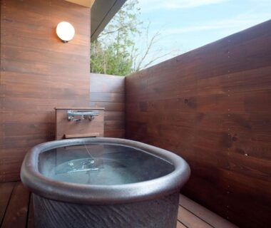 Outdoor wooden soaking tub on balcony with faucet and surrounding wooden walls