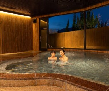Two guests relaxing in indoor onsen bath with wooden walls and garden view at Ooedo Onsen Monogatari Premium Enakyo Gifu