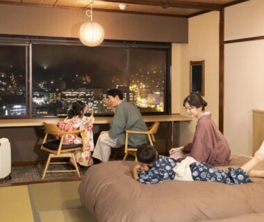 Family in yukata relaxing on futon beds and tatami floor with night city view at Ooedo Onsen Monogatari Gero