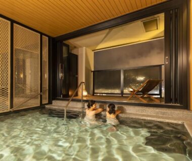 Two guests relaxing in a wooden indoor onsen bath with large window at Ooedo Onsen Monogatari Premium Gero Honkan Gifu