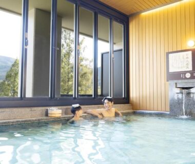 Two guests bathing in indoor onsen with large windows and mountain view at Ooedo Onsen Monogatari, Gifu
