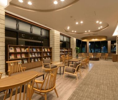 Wooden lounge with bookshelves and seating by large windows at Ooedo Onsen Monogatari Premium Ikaho, Gunma
