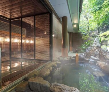 Steaming rock-lined onsen bath beside wooden screening at Ooedo Onsen Monogatari Premium Ikaho, Gunma