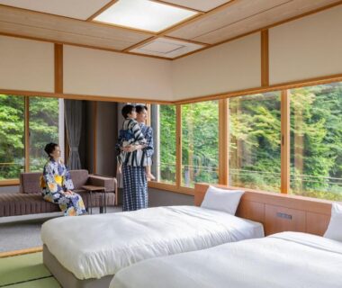 Tatami room with twin beds, shoji screens, large windows overlooking green hillside; guests in yukata