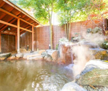 Steaming stone onsen bath with wooden shelter, rocks and garden wall at Ikaho ryokan in Gunma