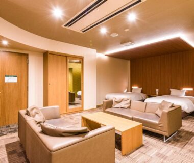 Carpeted guest room with twin beds, sofa seating and wood accents at Ooedo Onsen Monogatari Premium Ikaho, Gunma