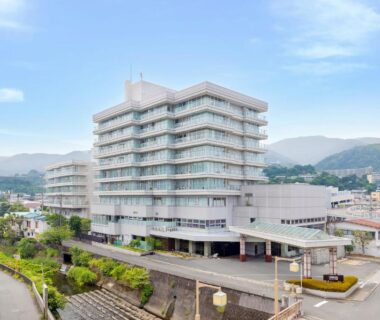 Multi-story hotel beside river with mountain backdrop in Ito Shizuoka at Ooedo Onsen Monogatari