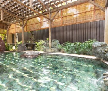 Covered outdoor onsen with stone edging and wooden roof at Ooedo Onsen Monogatari Ito, Shizuoka