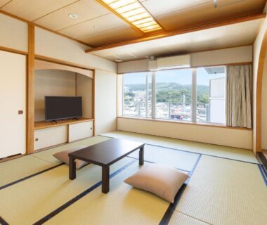 Tatami room with low table, floor cushion, TV and large window overlooking town and distant hills in Shizuoka