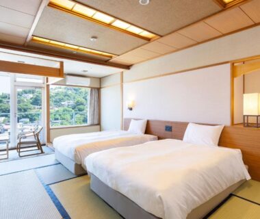 Tatami room with twin beds and balcony overlooking greenery at Ooedo Onsen Monogatari Premium Ito Hotel New Okabe, Shizuoka