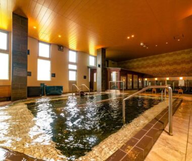 Spacious indoor communal bath with tiled edging and handrail at Ooedo Onsen Monogatari Premium Kinosaki Hyōgo