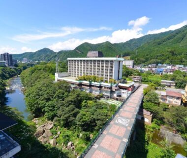 Long pedestrian bridge leading to a riverside multi-story hotel with green mountain backdrop in Kinugawa, Tochigi