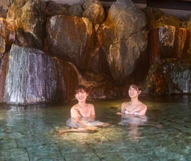 Two guests bathing in indoor onsen with rock waterfall backdrop at Ooedo Onsen Monogatari Premium Kinugawa Kanko Hotel Tochigi