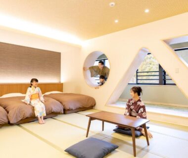 Tatami room with low table, futon beds, large windows and guests wearing yukata at Yamanaka ryokan