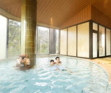 Guests relaxing in a spacious indoor onsen bath with tiled pillar and large windows at Yamanaka hotel