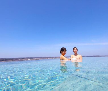 Two guests bathing in outdoor onsen pool with clear blue sky and distant horizon