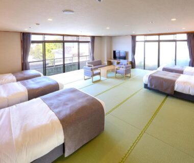 Large tatami-floored guest room with multiple beds, seating area and wide windows at Ooedo Onsen Monogatari Premium Yamashitaya, Ishikawa