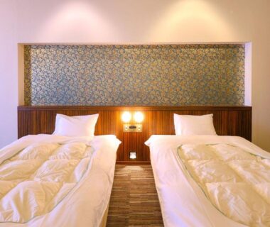 Twin beds with white duvets and wooden headboard at Ooedo Onsen Monogatari Premium Yamashitaya in Ishikawa