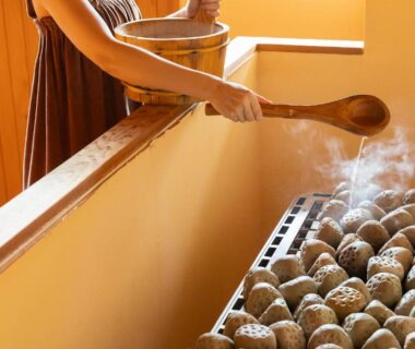 Hands pouring water over steaming onsen stones at Ooedo Onsen Monogatari Premium Yoshinoya Irokuen, Ishikawa