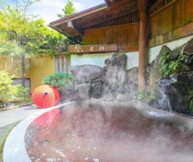 Steaming outdoor onsen bath with rock cascade and red umbrella at Ooedo Onsen Monogatari Shinshu Kakeyu, Nagano