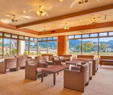 Bright lounge with sofas and low tables facing wide windows with mountain views near Saga, Kyūshū