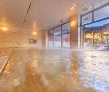 Tiled indoor onsen bath with handrail and large windows overlooking outdoor area at Ooedo Onsen Monogatari Ureshinokan Saga
