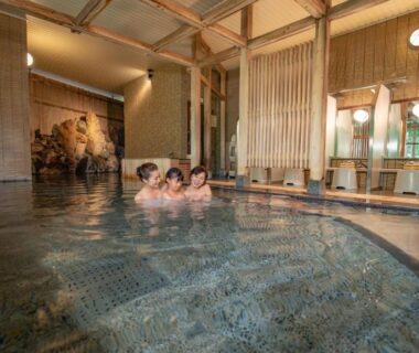 Guests relaxing in indoor onsen bath with tiled floor, wooden columns and shoji-style windows at Yamanaka Saichoraku