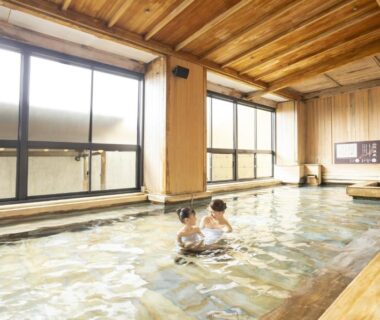 Two guests in spacious indoor wooden onsen with large windows at Ooedo Onsen Monogatari Yamashiro Saichoraku Ishikawa