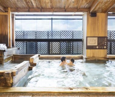 Guests soaking in a wooden indoor onsen bath with lattice windows at a ryokan in Ishikawa