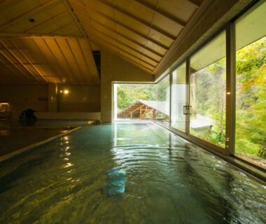 Indoor onsen bath with large windows overlooking green forest at Ookawaso, Fukushima