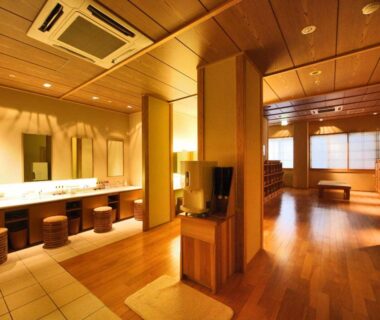 Warm wooden bathhouse dressing area with mirrors, washbasins, stools and benches at Ookawaso, Fukushima