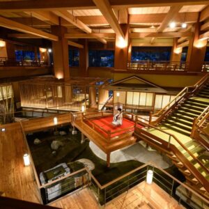 Grand wooden lobby with indoor water feature, staircases, shoji screens and warm lighting at Ookawaso, Tōhoku