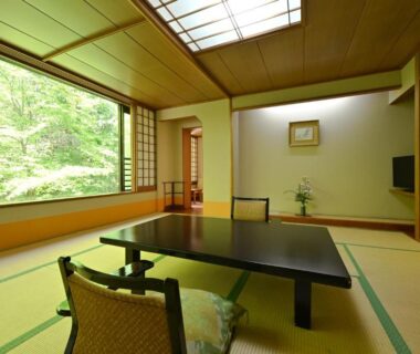 Traditional tatami room with low lacquer table, zabuton cushions, shoji window and garden view at Osakaya Ryokan, Gunma, Japan