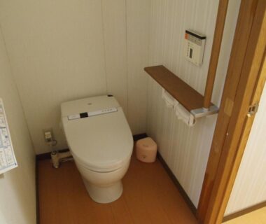 Compact toilet room with bidet-equipped toilet, wooden flooring and shelf at Oshi Ryokan, Nagano