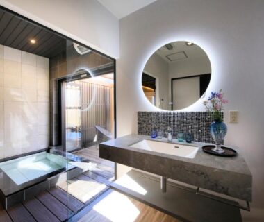 Modern ryokan bathroom with sunken wooden tub, backlit round mirror, stone vanity, and wood decking at Otogitei Kofu Nagano