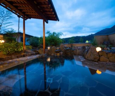 Stone outdoor onsen beneath a wooden roof at Otogitei Kofu in Nagano mountains