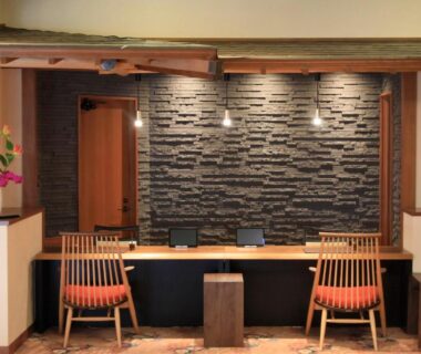Wooden reception counter with stone wall, pendant lights and two chairs in Otogitei Kofu lobby