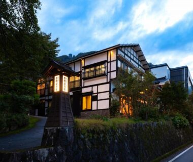 Twilight exterior of Otowaya Ryokan with lit lantern, timber framed facade, stone wall and garden path in Niigata