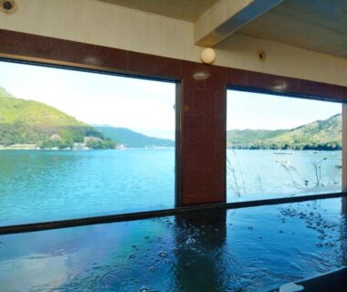 Indoor bathing pool with wide windows framing a calm bay and green hills at Owase Seaside View, Mie
